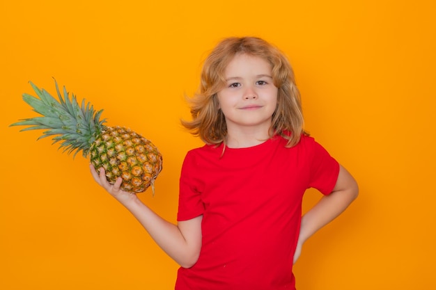 Cara de criança com frutas Garoto com abacaxi no estúdio Retrato de estúdio de uma criança fofa segurando abacaxi isolado em fundo amarelo