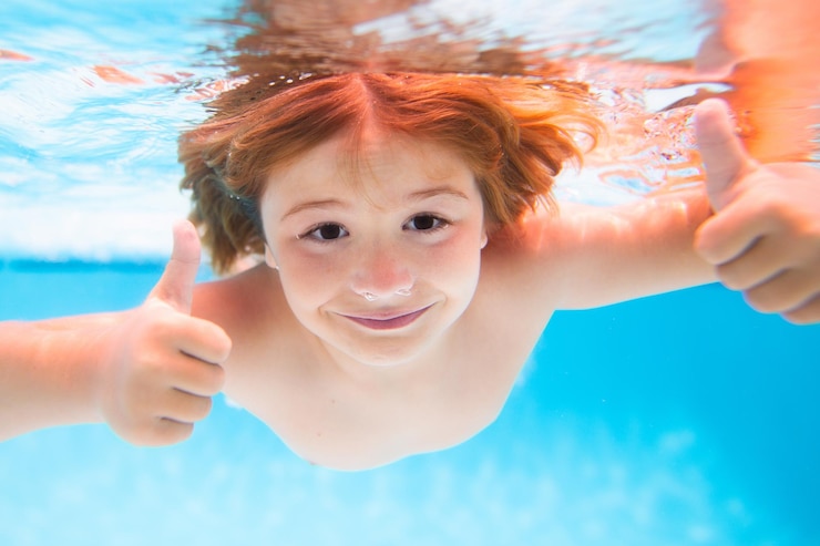 Foto cara de criança debaixo d'água com polegares para cima criança subaquática nada na piscina criança saudável nadando e tendo