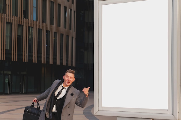 Foto cara de empresário amigável positivo para apresentação ou publicidade de produto, marca, logotipo no site ou cartaz. jovem bonito de terno em um outdoor vazio no contexto de um prédio comercial