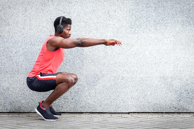 Cara de esportes afro-americanos malhando com fones de ouvido ao ar livre contra a parede