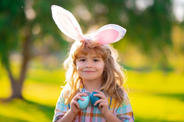 Cara de menino de criança de coelho Menino de caça aos ovos de páscoa Menino de criança com ovos de páscoa e orelhas de coelho no parque