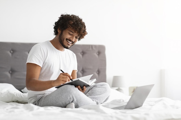 Cara de pele escura de pijama usando laptop tomando notas