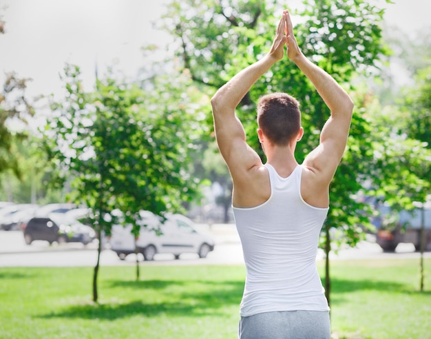 Cara desportivo praticando ioga ao ar livre, vista traseira. Jovem fazendo exercícios respiratórios na grama verde do parque, copie o espaço