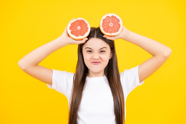 Cara divertida Chica adolescente feliz mantenga pomelo naranja aislado sobre fondo amarillo niños frutas vitamina