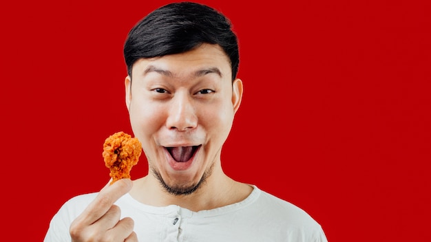 La cara divertida y feliz del hombre asiático está comiendo pollo frito deliciosamente