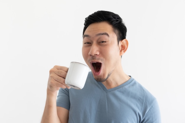 La cara divertida del hombre en camiseta azul bebe café de la taza blanca.