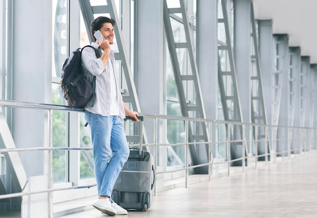 Cara do milênio falando no telefone esperando o voo com bagagem no aeroporto
