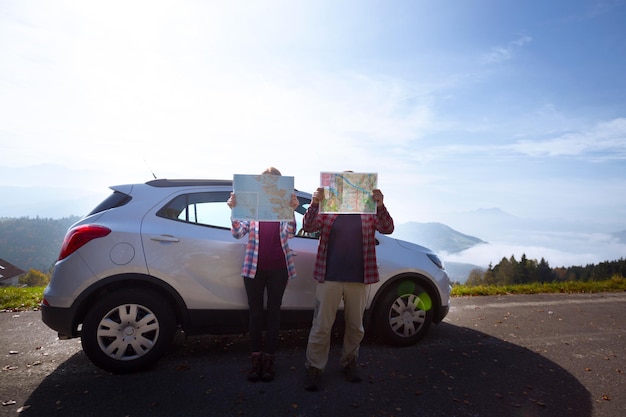 cara e garota parados ao lado do carro e olhando mapas em um fundo de montanhas viajam de carro