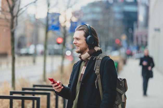 Cara elegante de cachecol e casaco ouve uma música no serviço de streaming usando telefone celular na rua de wroclaw polônia