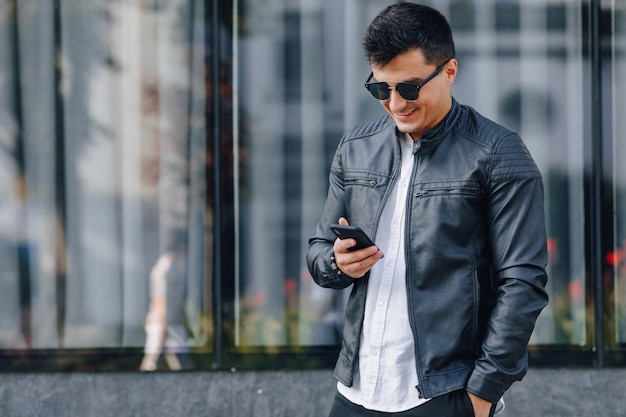 Cara elegante jovem de óculos na jaqueta de couro preta com telefone