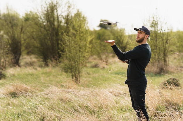 Foto cara em roupa totalmente preta com controle remoto e voando em um drone com fundo de campo