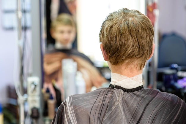 Cara em uma barbearia sentado na frente de um espelho