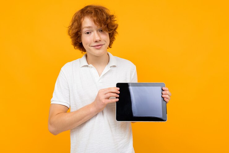 Foto cara encaracolada ruiva em uma camiseta branca mostra uma tela de tablet com um layout em uma parede amarela