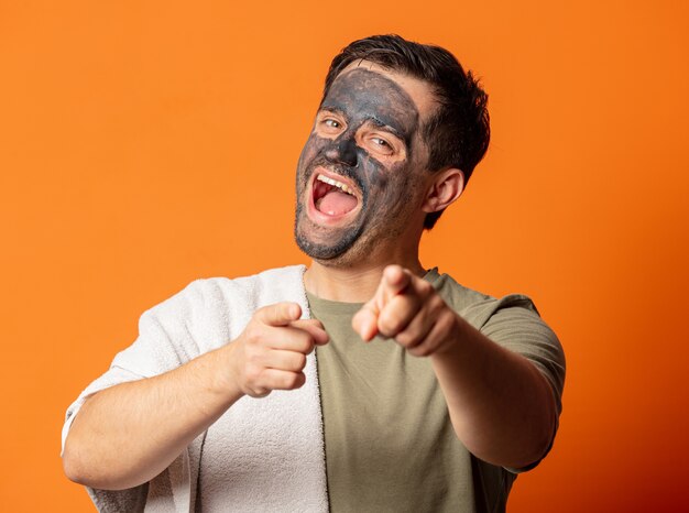 Cara engraçado com uma máscara cosmética no rosto e uma toalha laranja