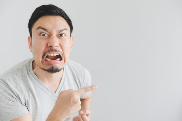 Cara enojada del hombre en camiseta gris con el punto de la mano en espacio vacío.