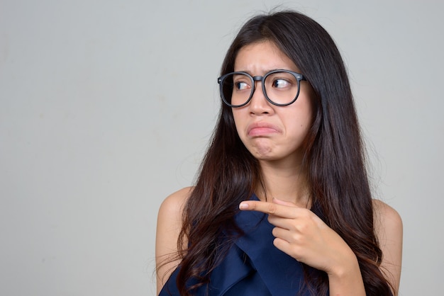 Cara de estresada joven empresaria asiática apuntando hacia un lado y mirando disgustado