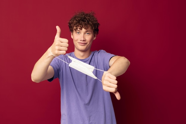 Cara excêntrico em camiseta roxa máscara médica nas mãos segurança fundo vermelho inalterado