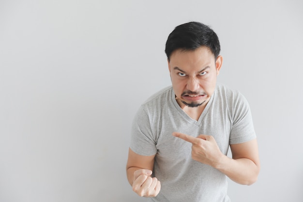 Cara feia do homem em t-shirt cinza com ponto de mão no espaço vazio.