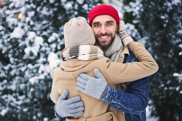 Cara feliz abraçando com namorada em madeira de neve