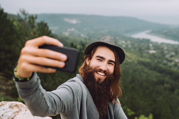 Cara feliz em alta montanha usando um telefone celular tira uma selfie.