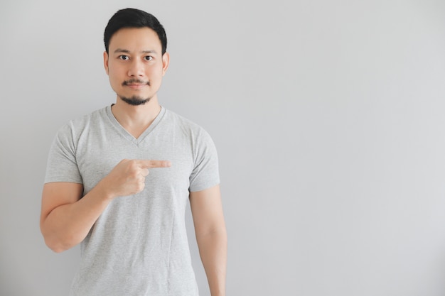 Cara feliz del hombre en camiseta gris con el punto de la mano en espacio vacío.