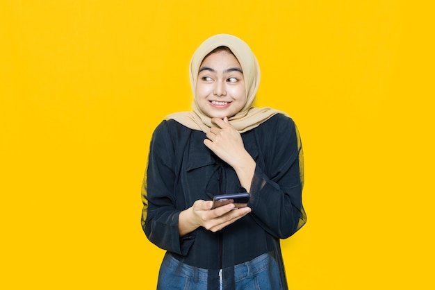 Cara feliz de joven asiática con smartphone en pared amarilla