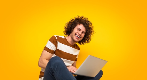 Cara feliz usando netbook e sorrindo para a câmera no estúdio amarelo