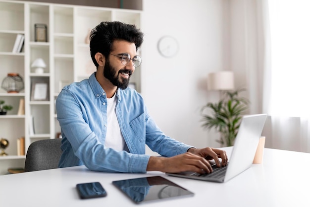 Foto cara freelancer indiano do milênio trabalhando on-line no laptop no escritório doméstico