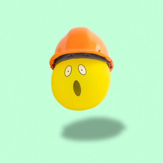 Foto cara de globo amarillo sorprendido con máscara de construcción flotando sobre fondo verde pastel