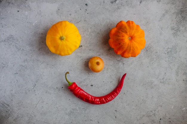 Una cara hecha de calabazas y un pimiento rojo.