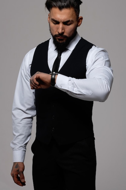 Foto cara hispânico barbudo de colete escuro e camisa branca com gravata olhando para a câmera com as mãos nos bolsos