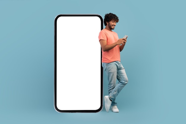 Cara indiano legal, apoiando-se em um smartphone enorme usando telefone celular