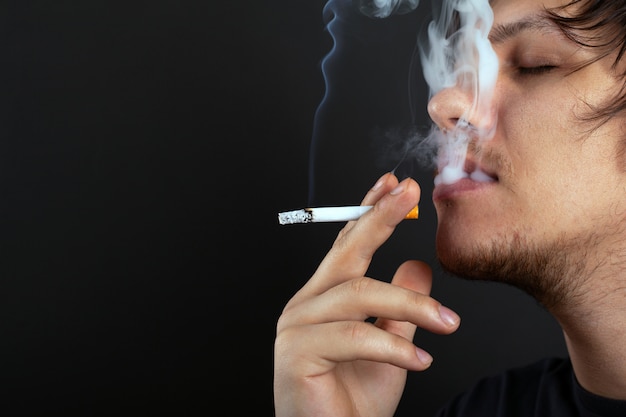 Foto cara jovem de barba por fazer fuma um cigarro no espaço branco da cópia de fumaça.