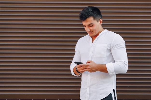 Cara jovem elegante na camisa digitando no telefone