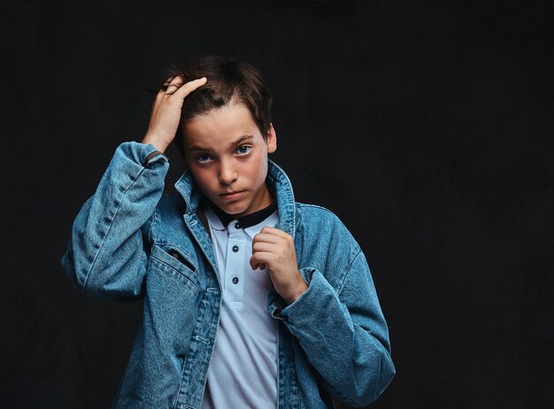 Cara jovem elegante vestido com uma camiseta e jaqueta jeans posando em um estúdio. Isolado no fundo escuro.