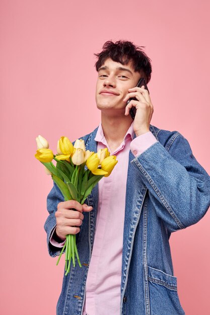 Cara jovem em uma jaqueta jeans com um buquê de flores falando ao telefone fundo rosa