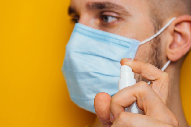 cara jovem em uma máscara em um amarelo. Desinfeta as mãos com um anti-séptico. Pulveriza o controle de pragas. conceito de coronavírus. Proteção contra germes e vírus.