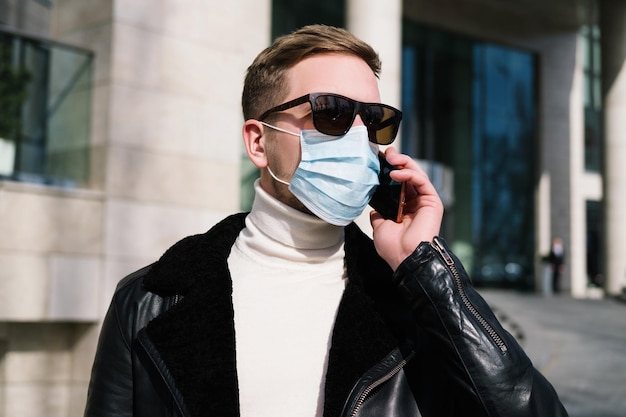 Cara jovem em uma máscara médica usa um telefone na rua, conceito de quarentena