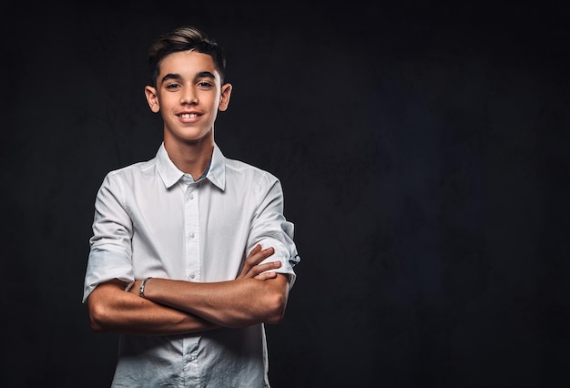 Cara jovem feliz vestido de camisa branca em pé com os braços cruzados. Isolado em um fundo escuro.