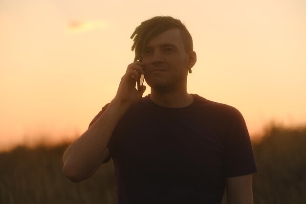Foto cara jovem sério tendo telefonema na zona rural ao pôr do sol