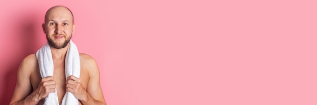 Cara jovem sorridente com um torso nu segurando uma toalha em volta do pescoço em um fundo rosa Banner
