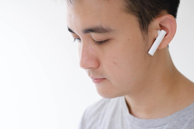 La cara de un joven asiático escuchando auriculares estéreo inalámbricos verdaderos blancos