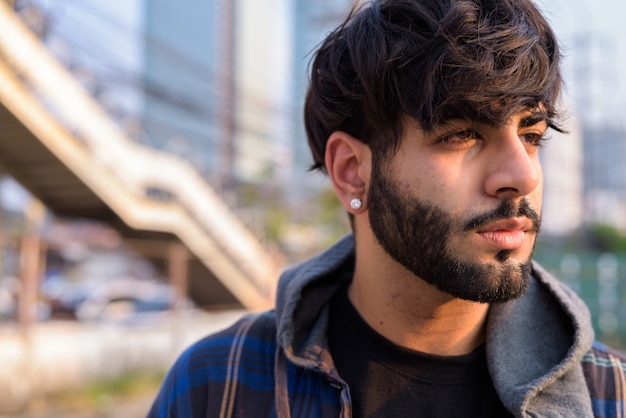 Cara de joven guapo hipster indio barbudo pensando en las calles de la ciudad al aire libre