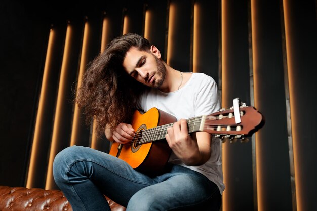Foto cara latino talentoso tocando guitarra sentado no estúdio preto escuro