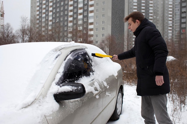 Cara limpa a neve com uma escova do carro um homem cuida do carro no inverno