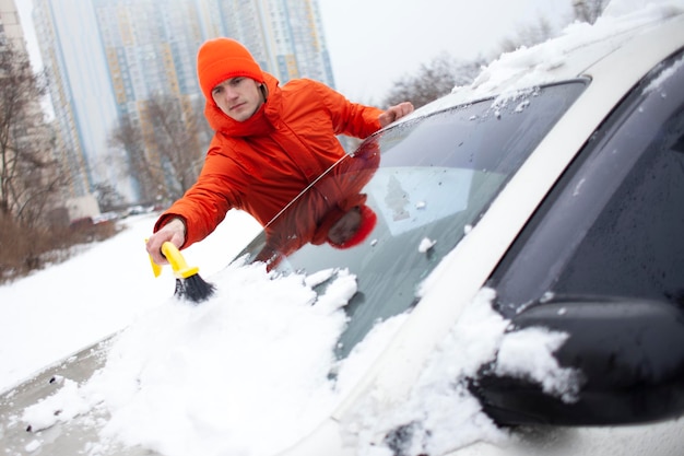 Cara limpa a neve com uma escova do carro um homem cuida do carro no inverno