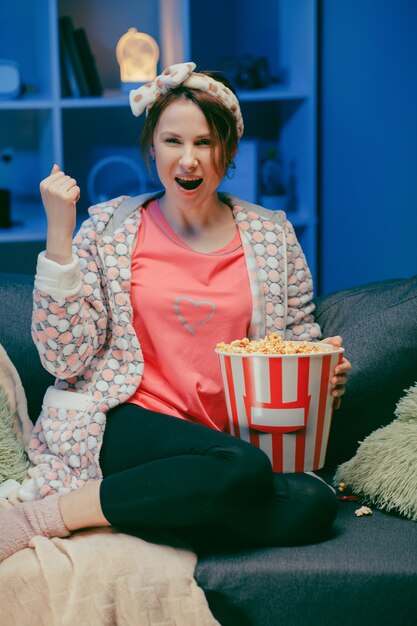 Foto cara linda garota feliz assistindo filme de comédia em casa. milenar mulher sentada no sofá e assistindo tv.