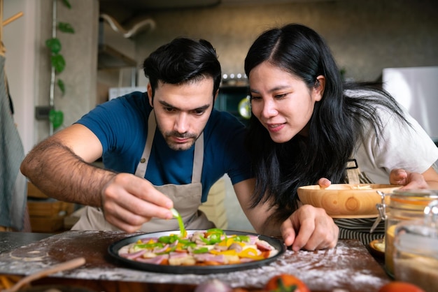 Cara de masa de pizza italiana casera con verduras y salsa cocinada por una pareja amorosa chef en casa en la mesa en la cocina moderna feliz momento familiar juntos