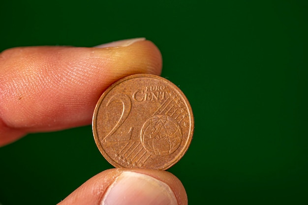 Foto cara de la moneda de 2 centavos de euro sostenida entre el pulgar y el dedo índice