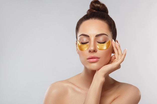 Cara de mujer de belleza con almohadillas doradas de colágeno debajo de los ojos Máscara antienvejecimiento para ojos Parches de hidrogel dorados para ojos